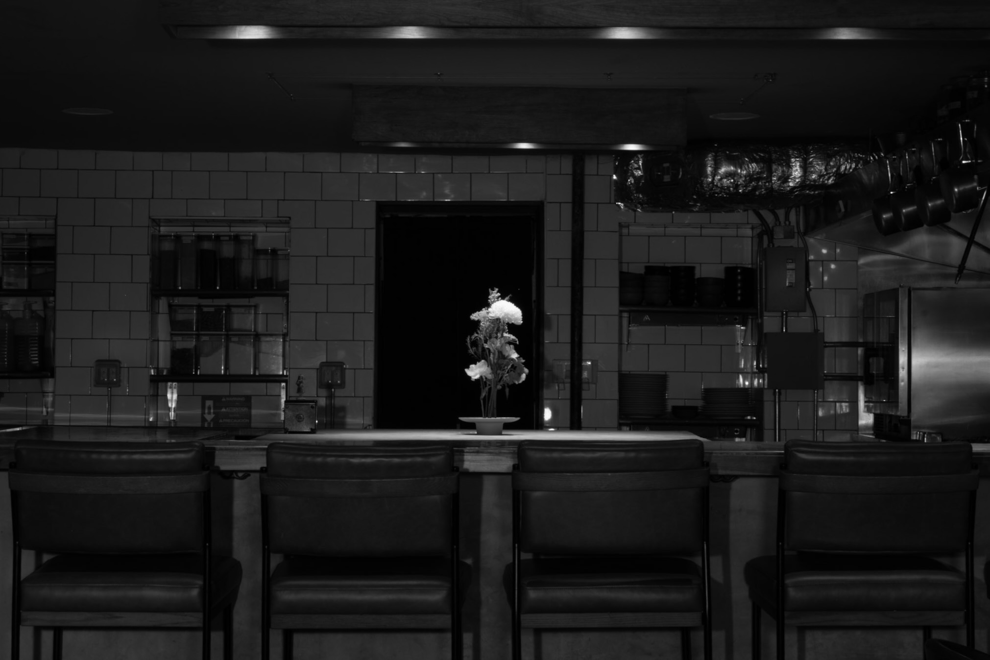 Corima chef's counter — leather bar stools along a tiled wall with a single spotlit floral arrangement on the counter