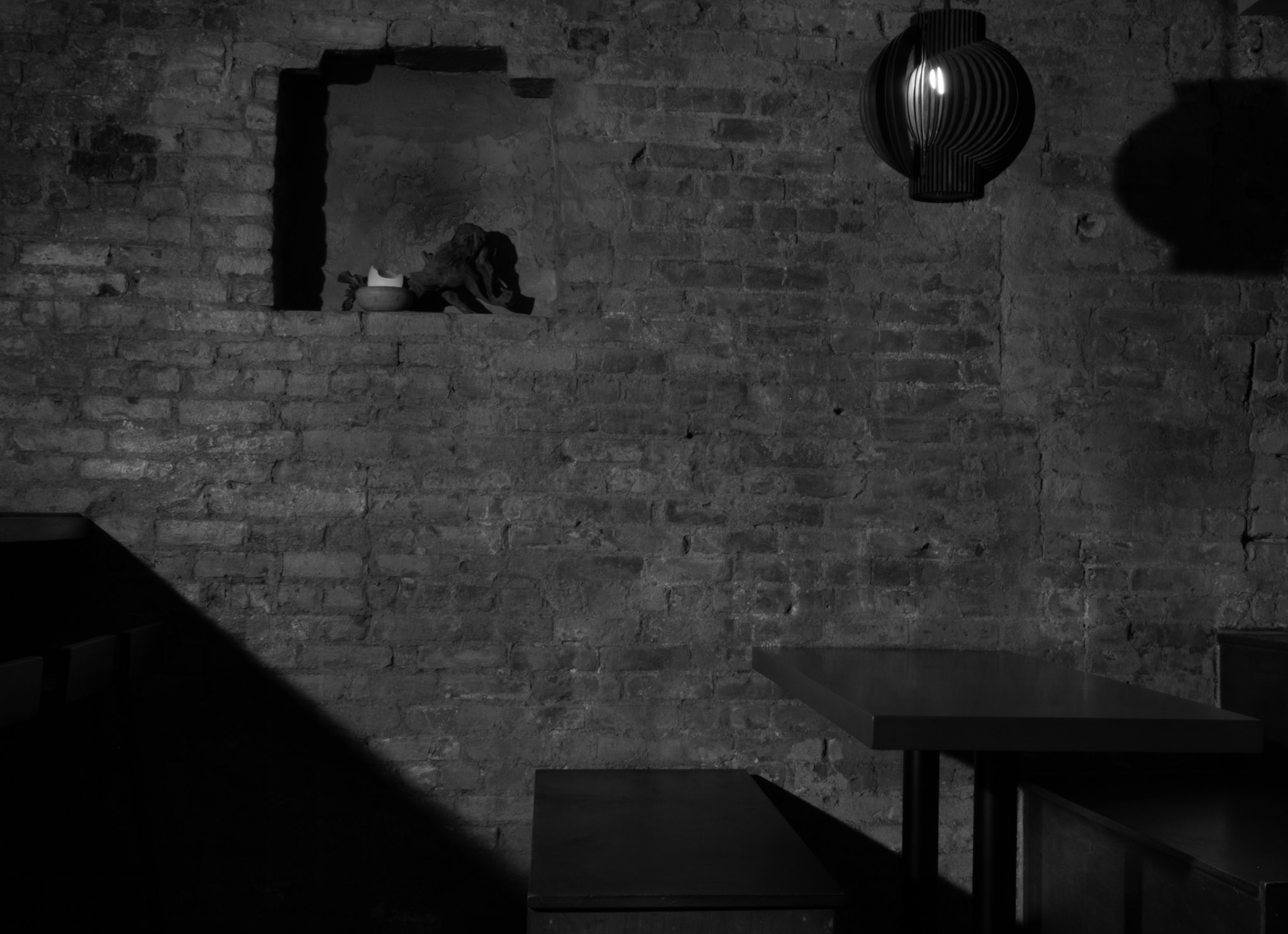 Corima dining room — exposed brick wall with a candle-lit niche, a ribbed globe pendant, and dark tables below